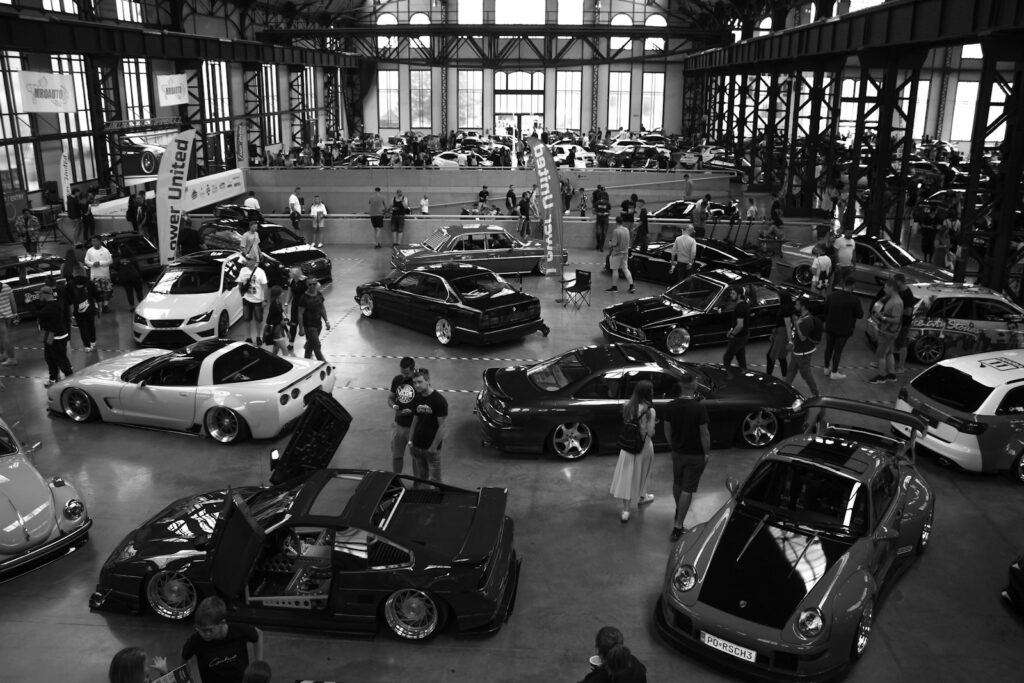 People gathered around custom cars at an indoor exhibition.