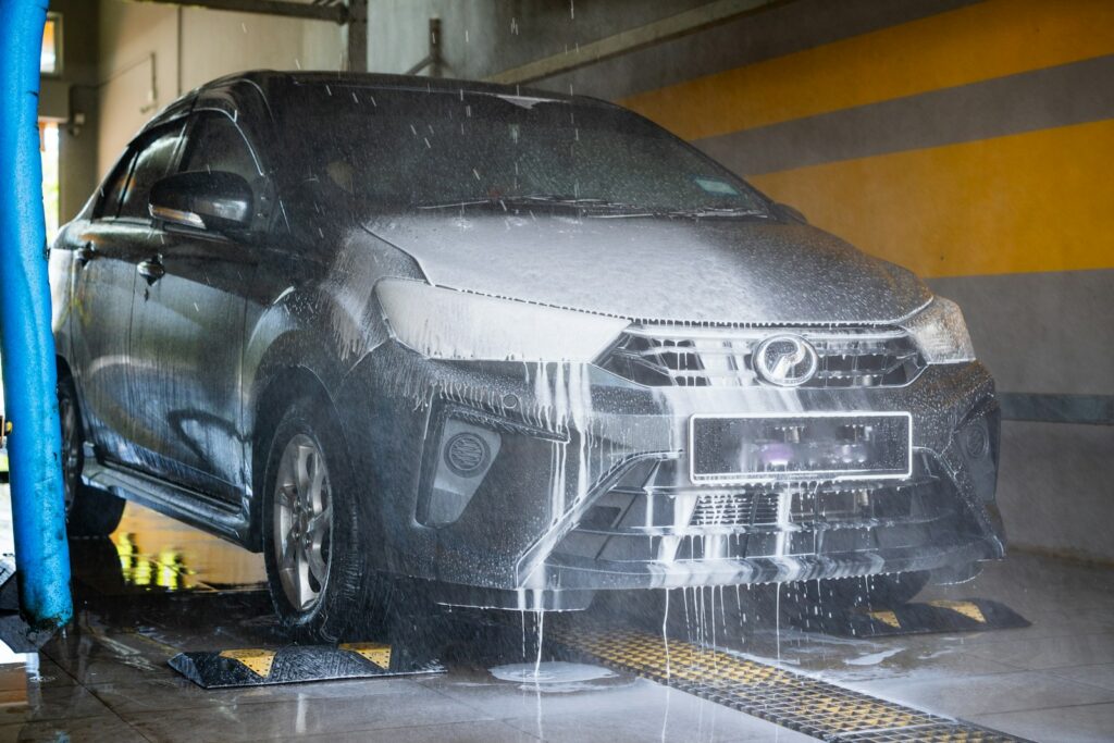 A dark car being washed with foam and water.