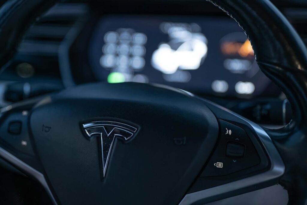 Detailed view of a Tesla steering wheel with dashboard display in focus, showcasing modern car interior design.