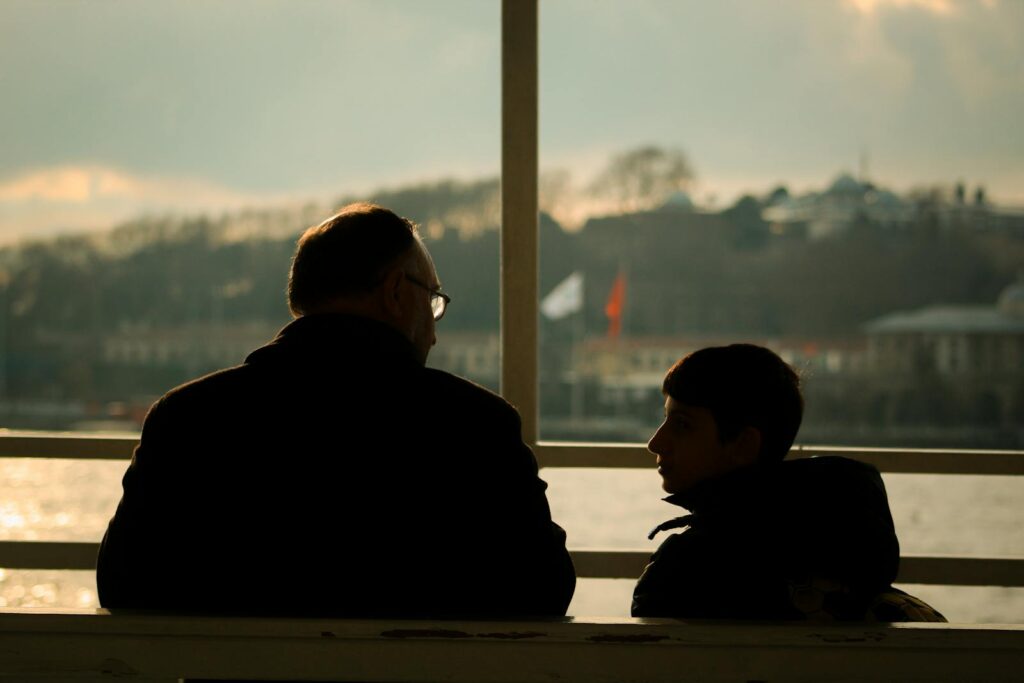A father and son share a moment sitting by the lakeshore at sunset, capturing family warmth.