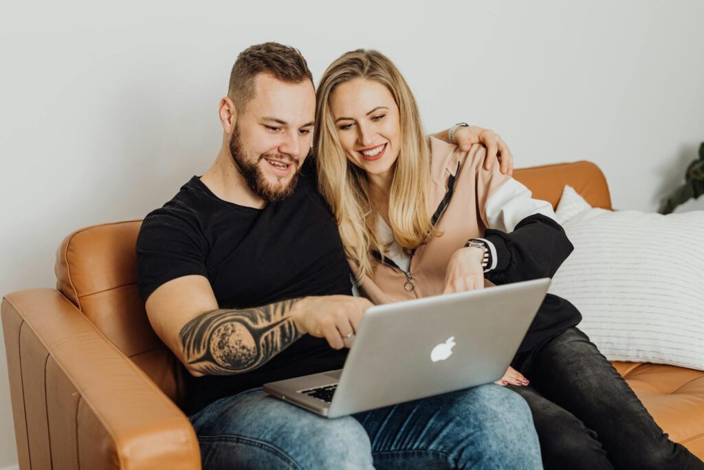 Happy couple enjoying time on couch using laptop together indoors.