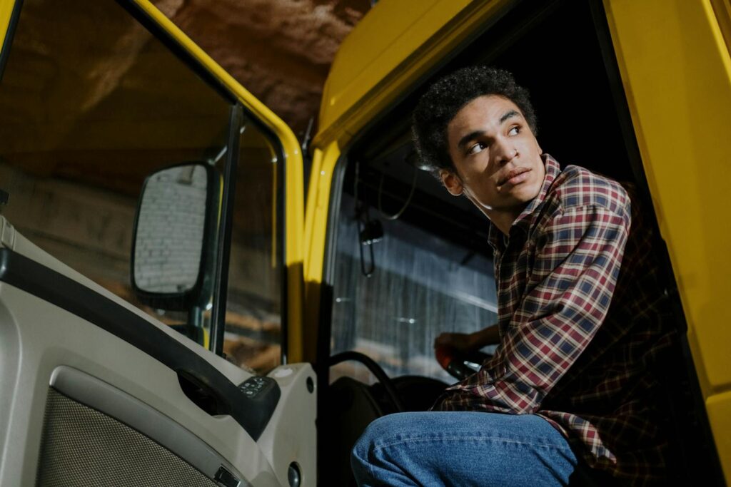 Young man in plaid shirt seated inside a truck cab, looking outside at night.