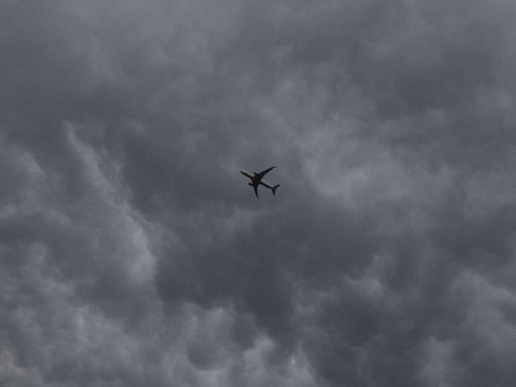 A silhouette of an airplane flying amidst dark storm clouds, showcasing aviation and weather phenomena.