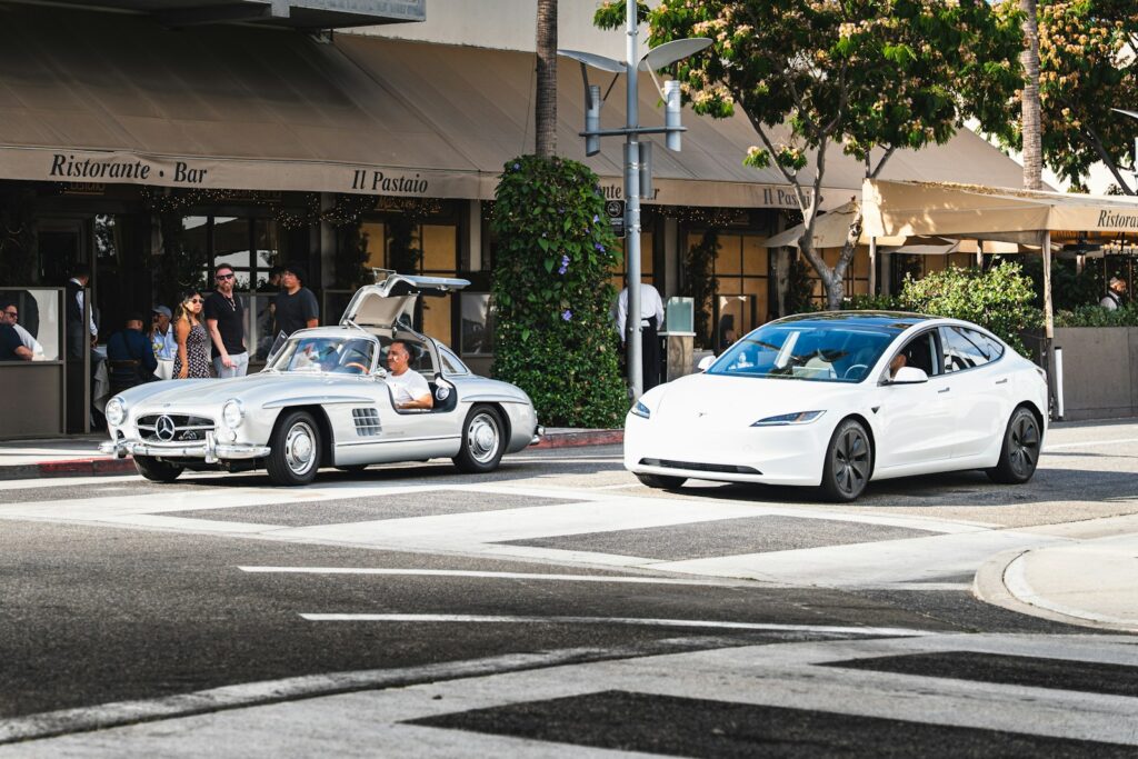 Classic silver mercedes and white tesla on street.