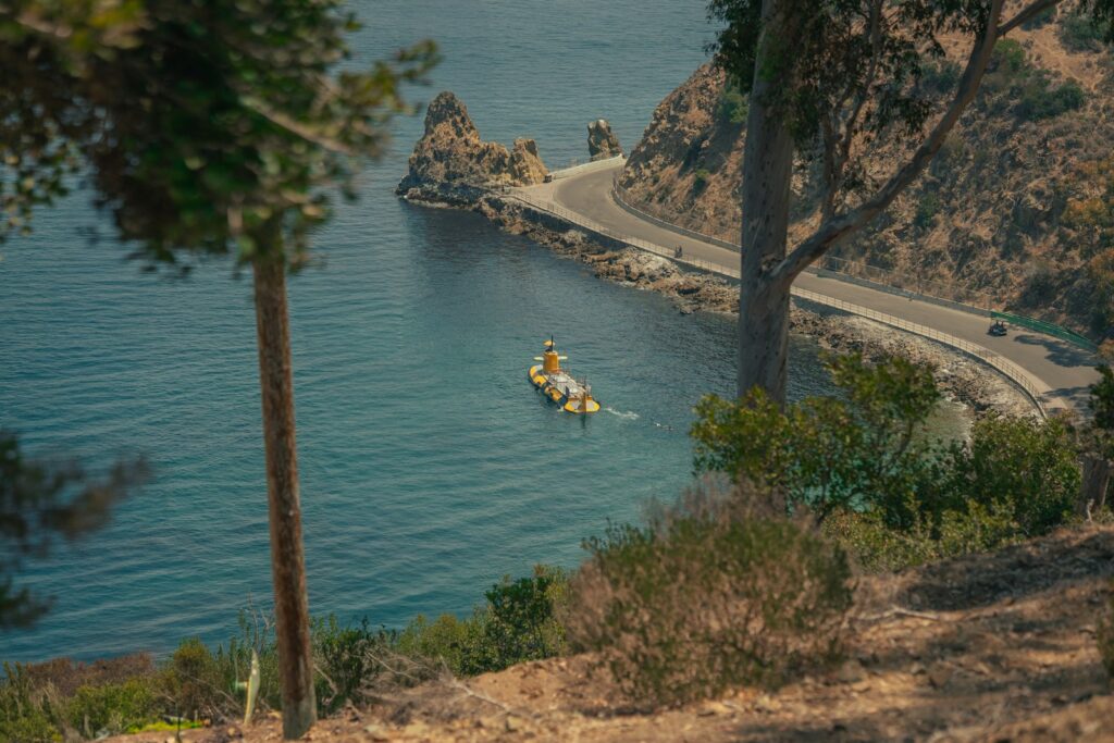 A boat floats on the calm blue water near a road.