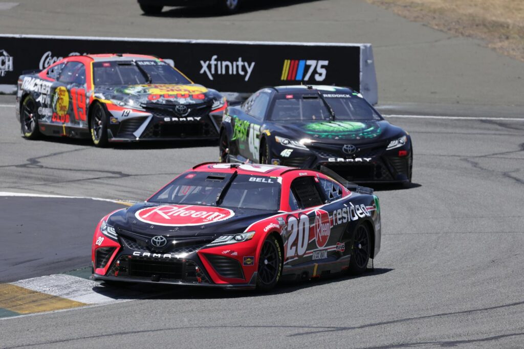 Dynamic stock car race with colorful vehicles speeding on a sunlit track at a major event.