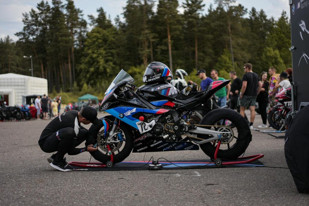 A man prepares a racing motorcycle at an outdoor event with spectators.