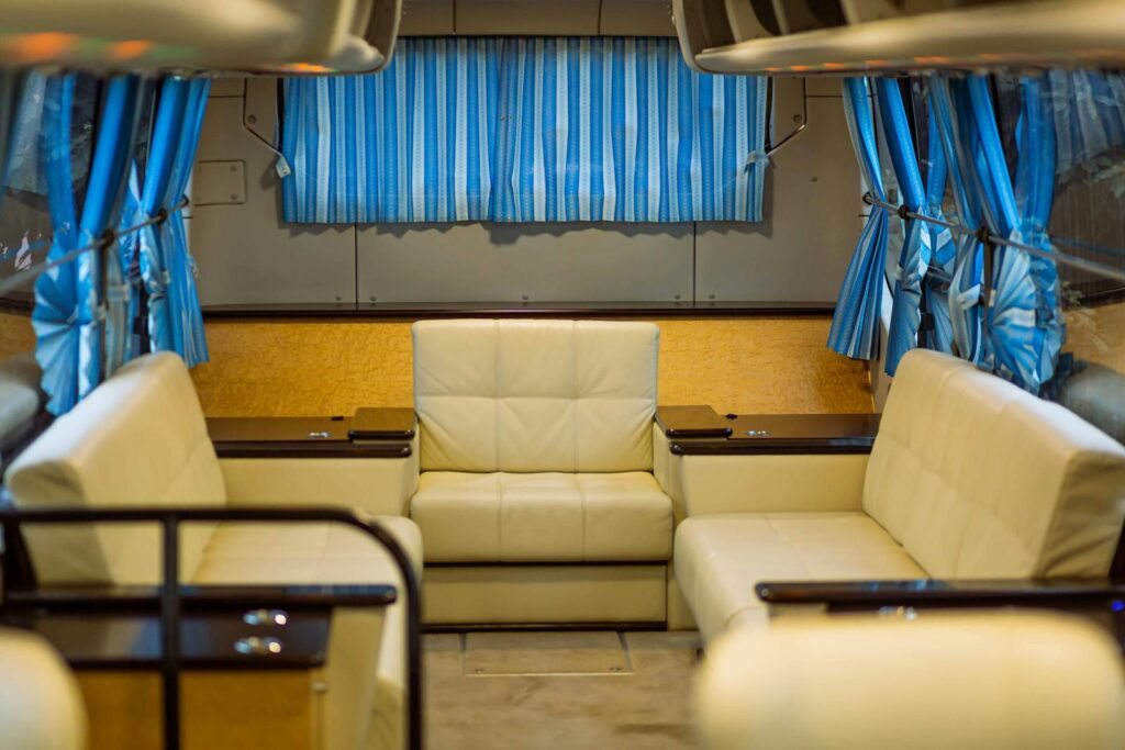 Spacious and luxurious van interior featuring leather seats and blue curtains.