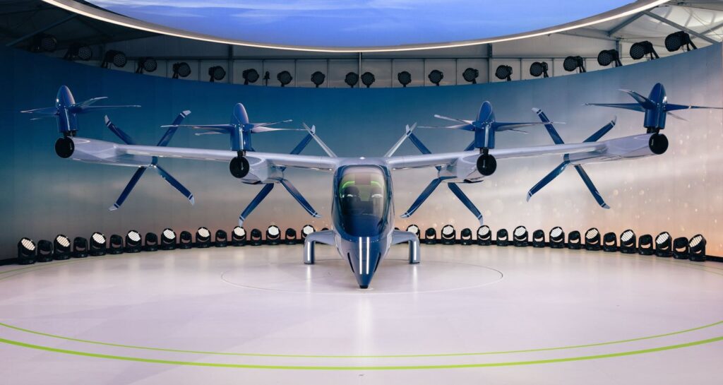 Front view of a futuristic electric vehicle with propellers displayed indoors.