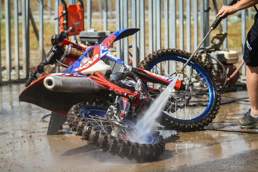 A motocross bike being pressure washed outdoors in Lombok, Indonesia, showcasing the cleaning process.