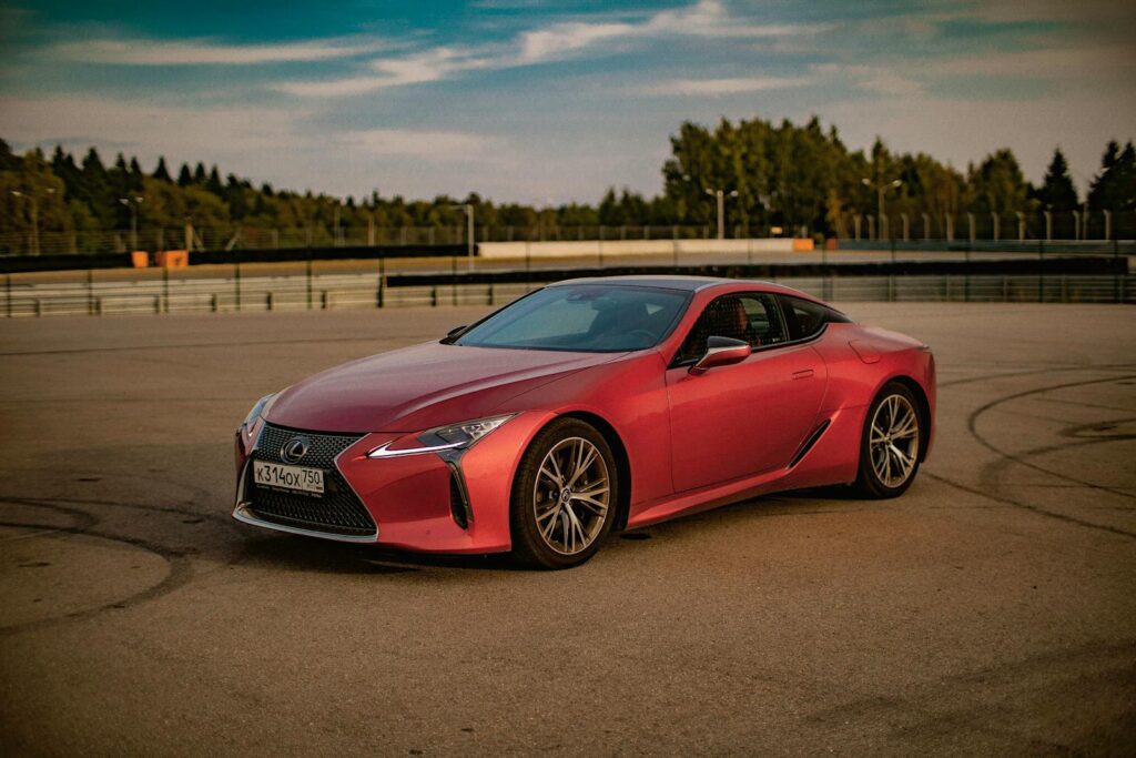 Red Lexus sports car parked on an empty race track under clear skies.