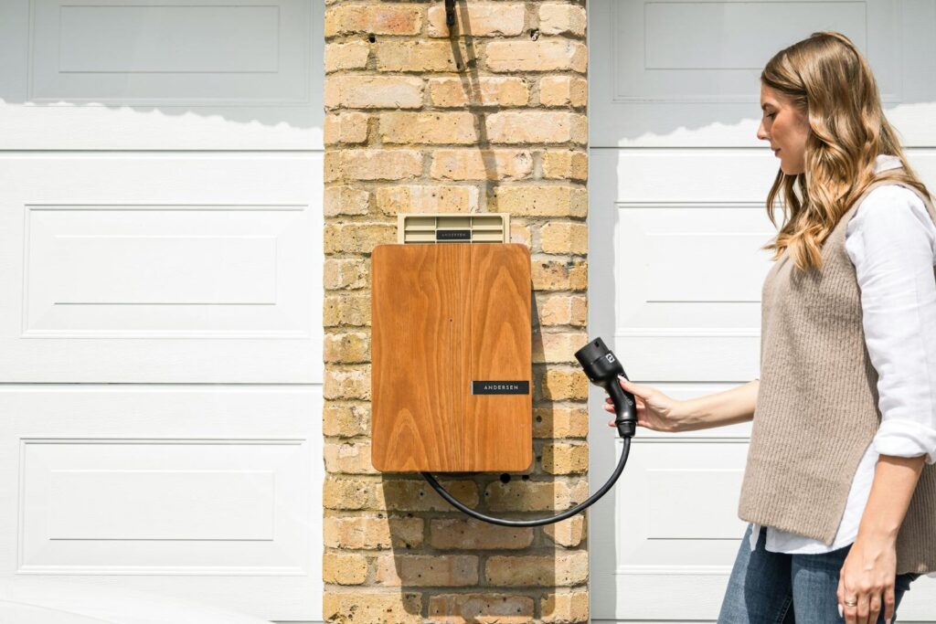 A woman uses a home electric vehicle charger mounted on a brick wall.