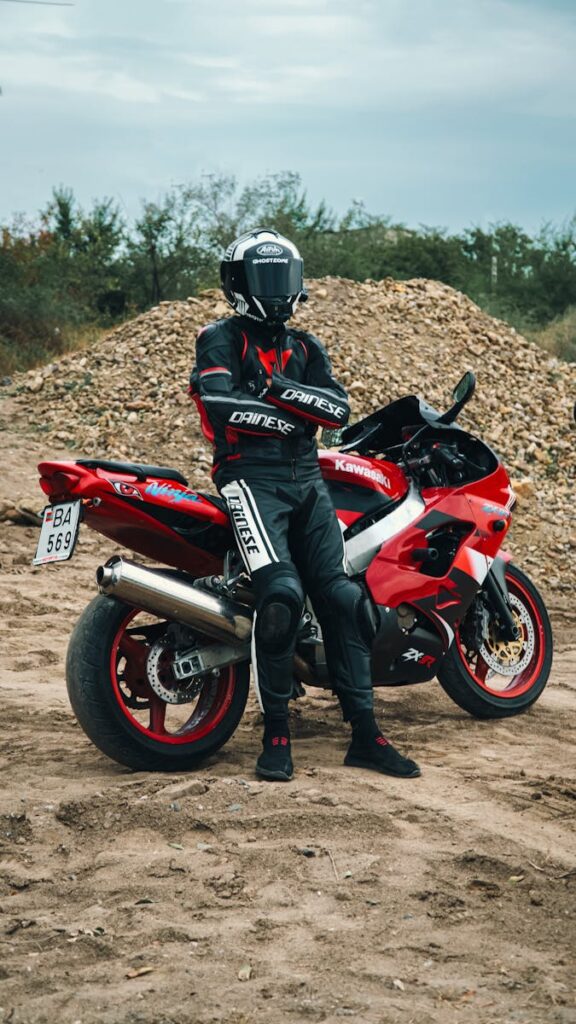 Motorcyclist in full gear standing by a red sport bike outdoors.