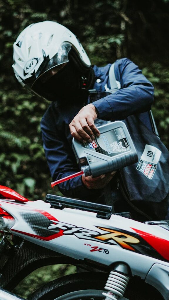 A person in motorcycle gear pouring engine oil into a motorbike in Jakarta, Indonesia.