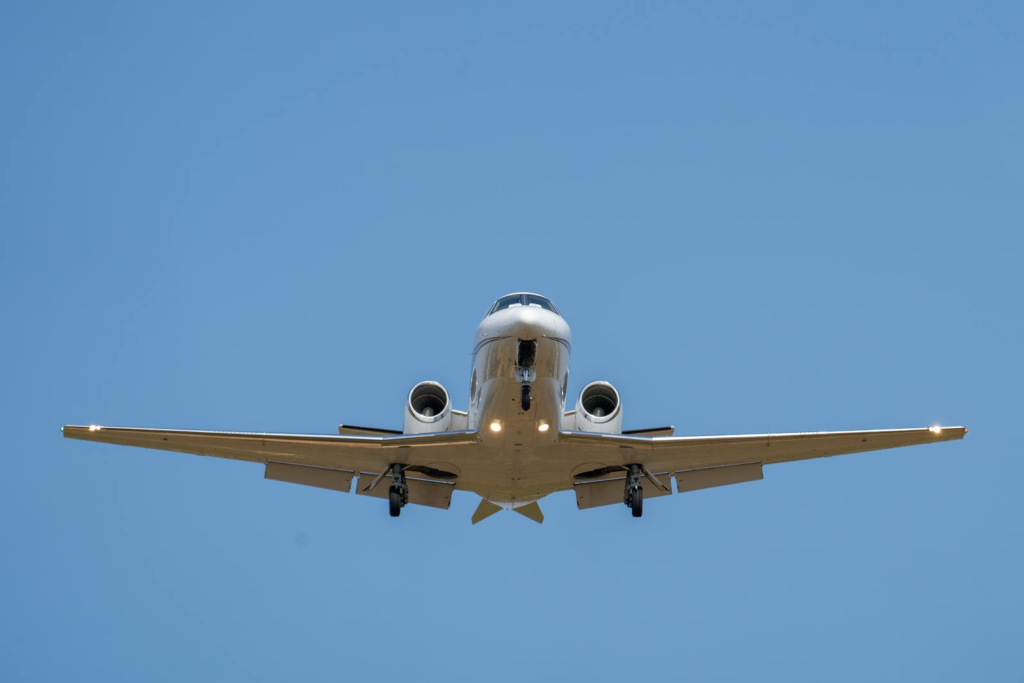 A private jet is captured flying overhead against a clear blue sky.