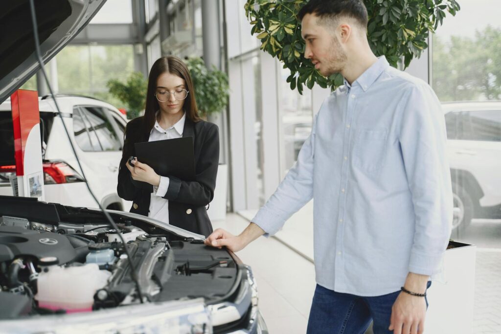 Man and woman examining car engine in dealership service area, focused on vehicle maintenance and functionality.