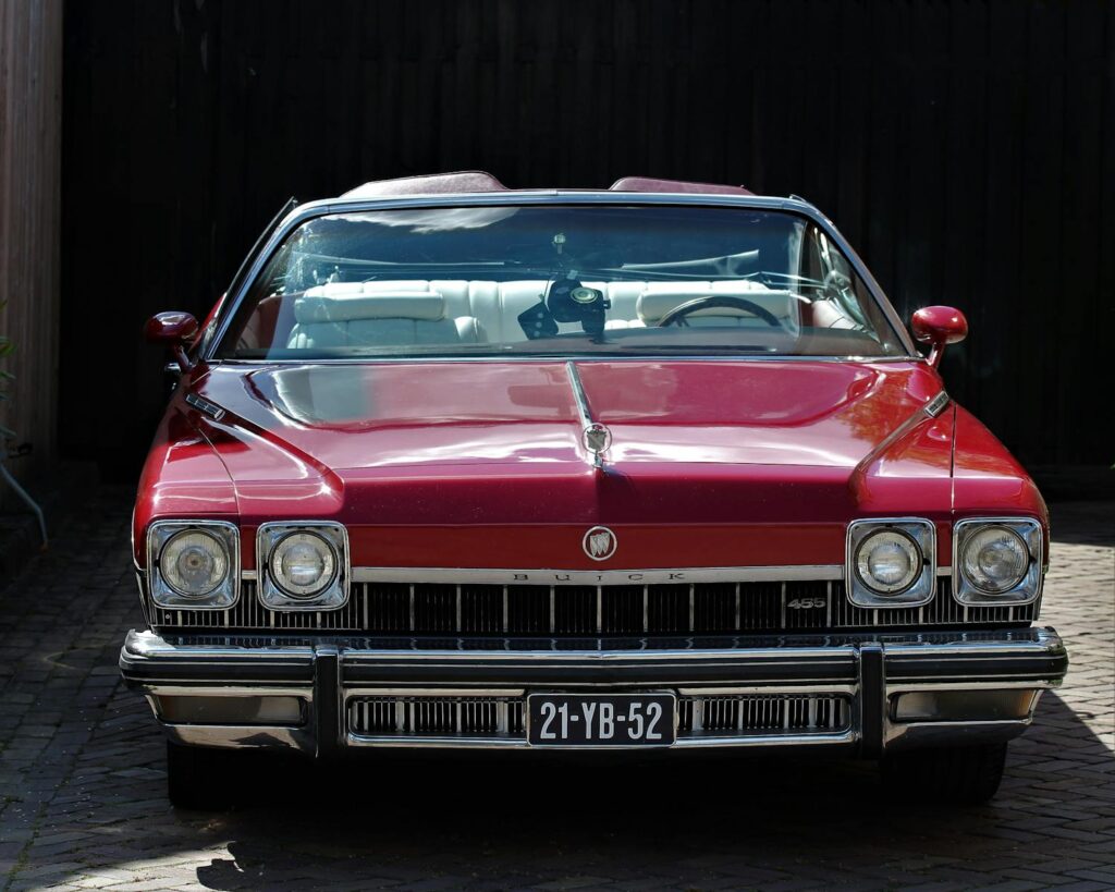 Classic red Buick convertible with license plate parked outdoors on a sunny day.