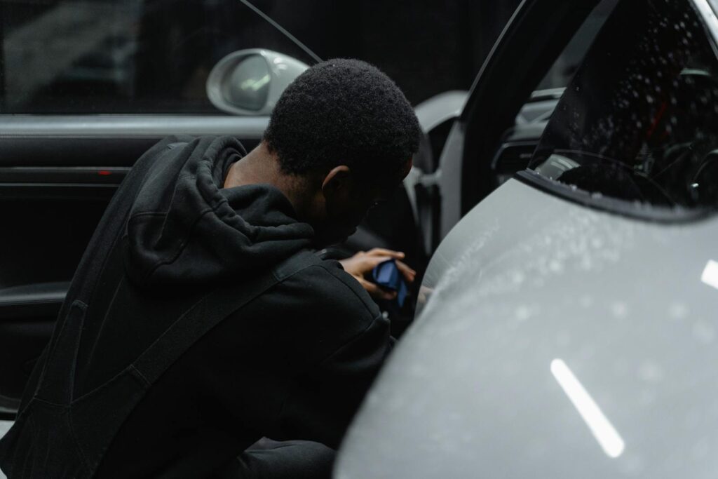 A person is meticulously detailing a luxury car interior under dim lighting, highlighting precision and care.