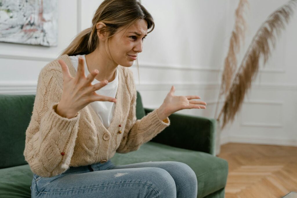 A woman sitting on a green sofa, gesturing emotionally, indoors.