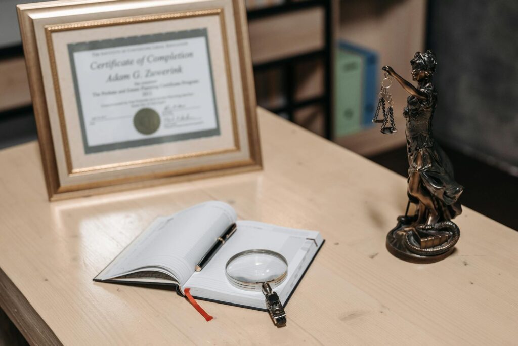 A framed certificate with Lady Justice statue on a wooden desk.