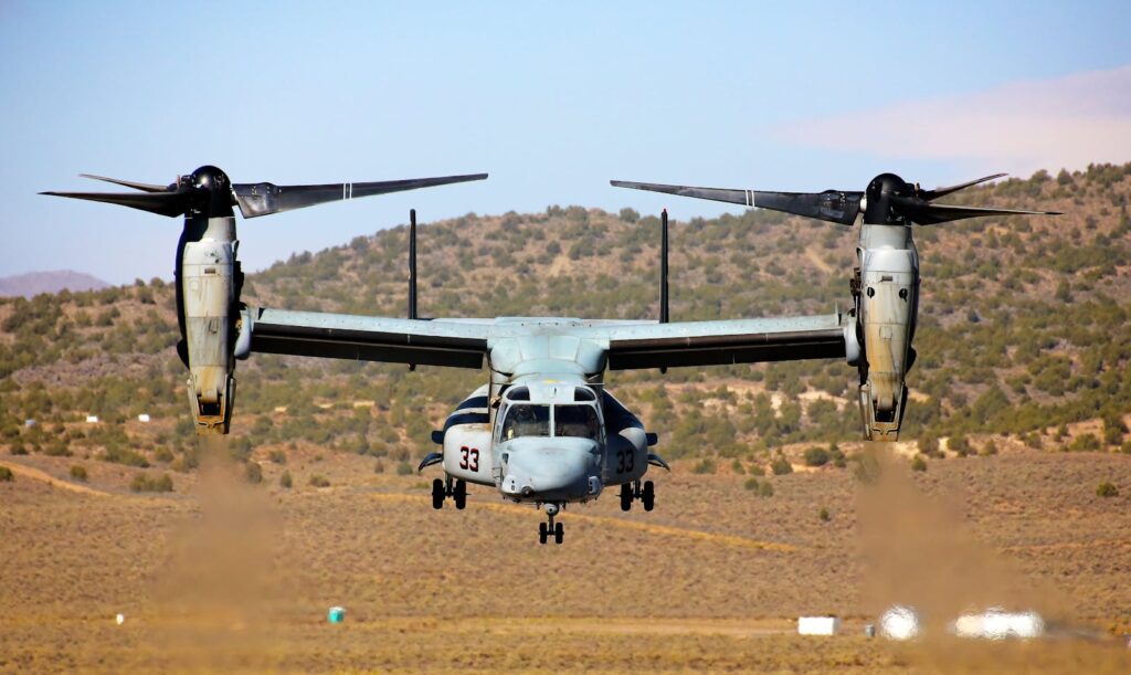Osprey aircraft flies over Nevada's desert landscape. Blue skies, propellers in motion.