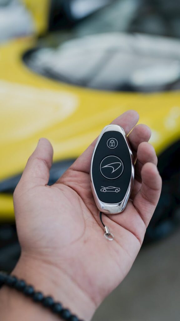 Close-up of a luxury car key held in a hand with a vibrant yellow car in the background.
