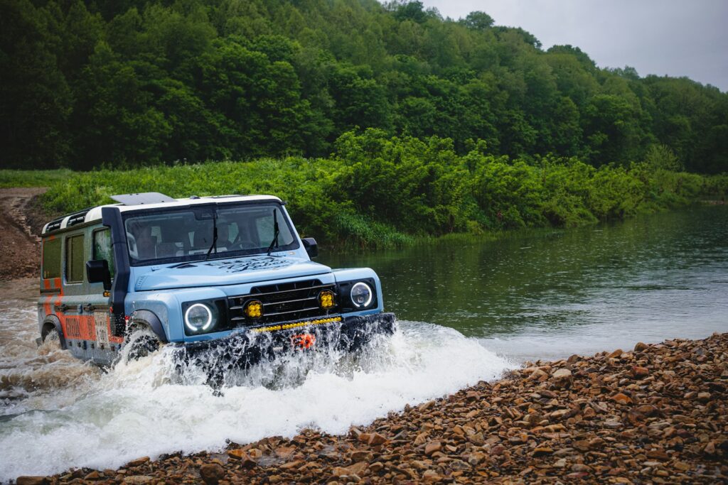 A blue jeep splashes through a river.