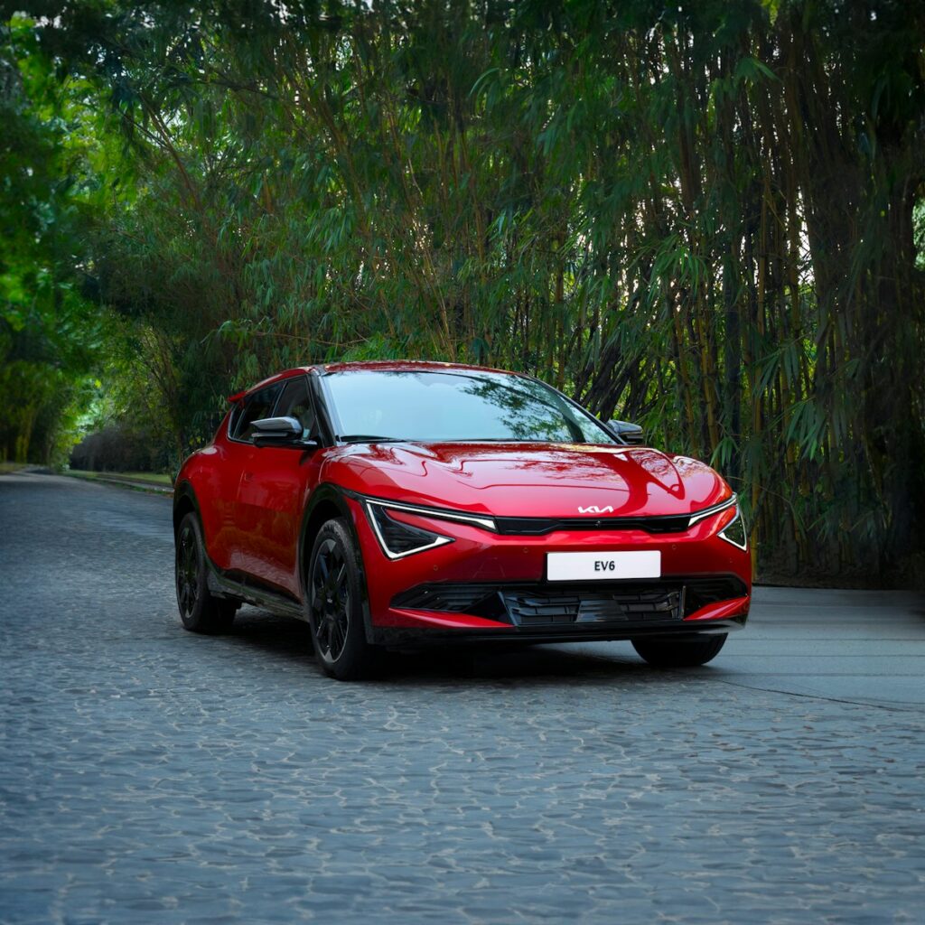 A red car driving down a street next to trees