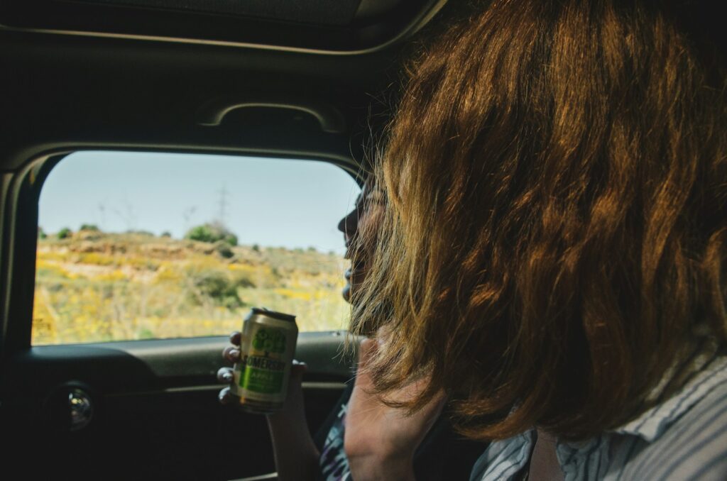 a woman sitting in the back of a car holding a can of beer