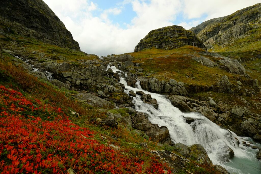 Rocky mountain landscape with a cascading waterfall and red foliage.