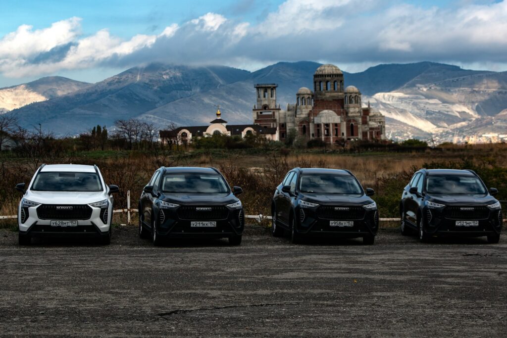 Four cars parked with a building and mountains behind.