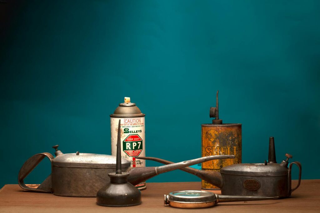 A collection of antique oil cans and vintage spray bottle against a green background in a studio.