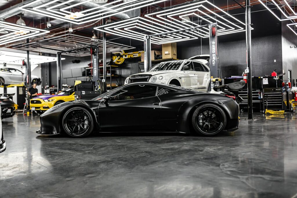 A sleek black sports car and luxury vehicles in a high-end auto repair shop interior.