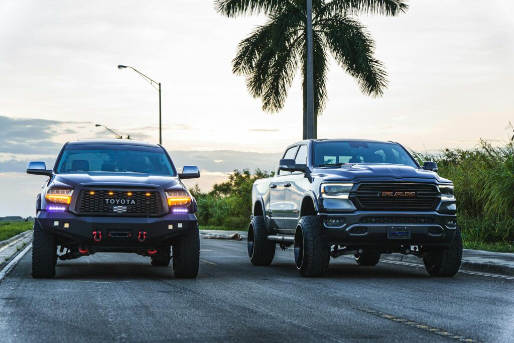 Two rugged pickup trucks parked on an open road by palm trees during dusk, showcasing power and style.