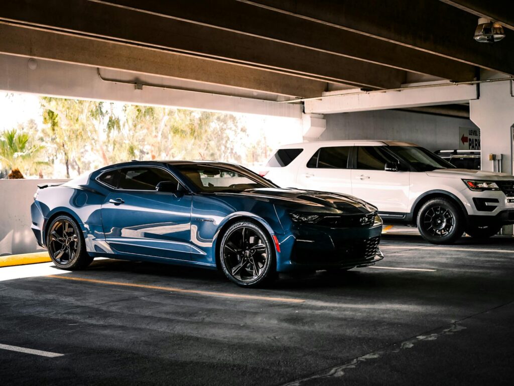 Luxurious blue sports car parked indoors beside a white SUV in urban garage setting.