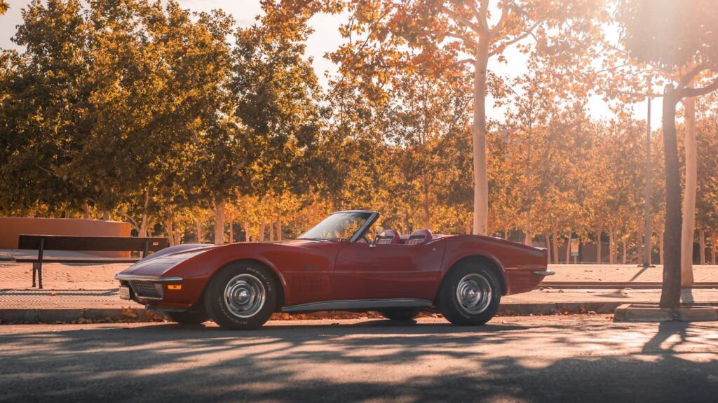 Vintage red convertible parked on a tree-lined street at sunset.