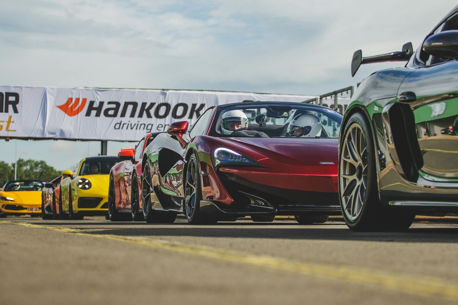 A lineup of high-performance sports cars ready for a racing event at a circuit.
