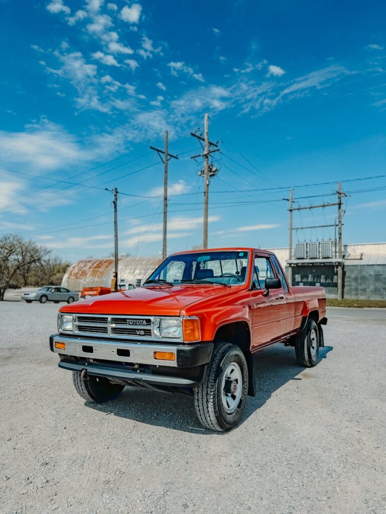 Bright red Toyota pickup truck parked outdoors against a blue sky in an industrial area.