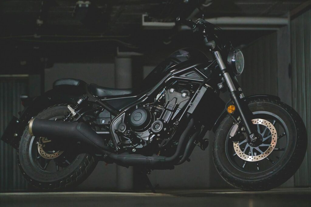 Close-up of a black Honda motorcycle in an industrial garage, showcasing detailed mechanics and design.