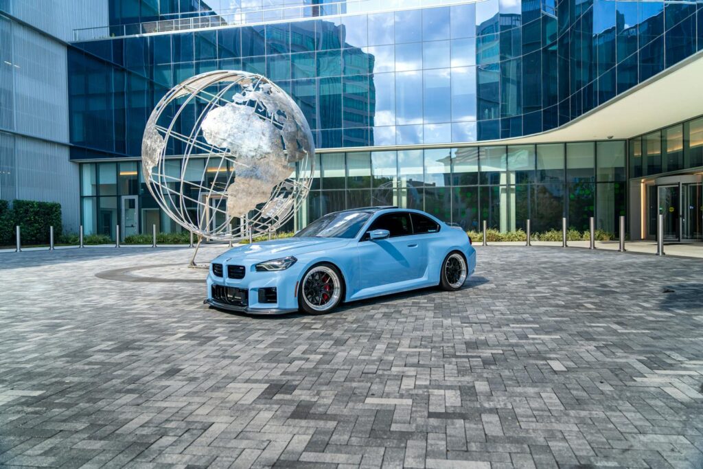 A sleek blue car in front of a globe sculpture and modern glass building, conveying urban sophistication.