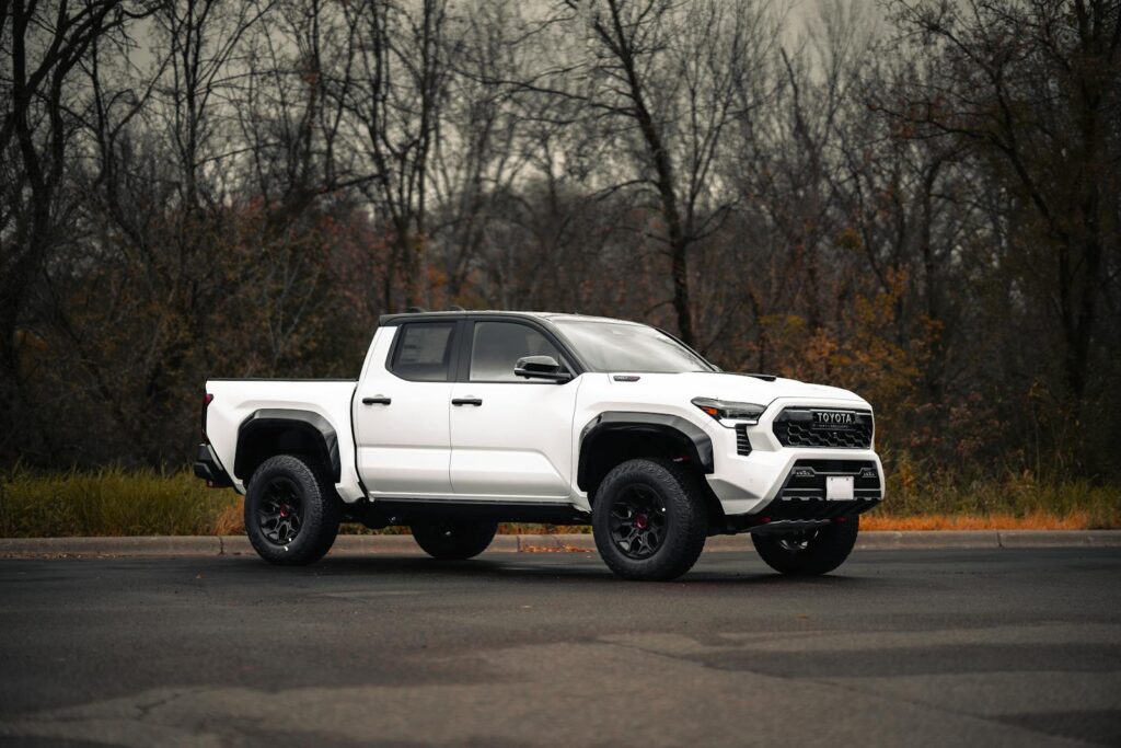 White pickup truck parked on an empty road with autumn trees in the background.