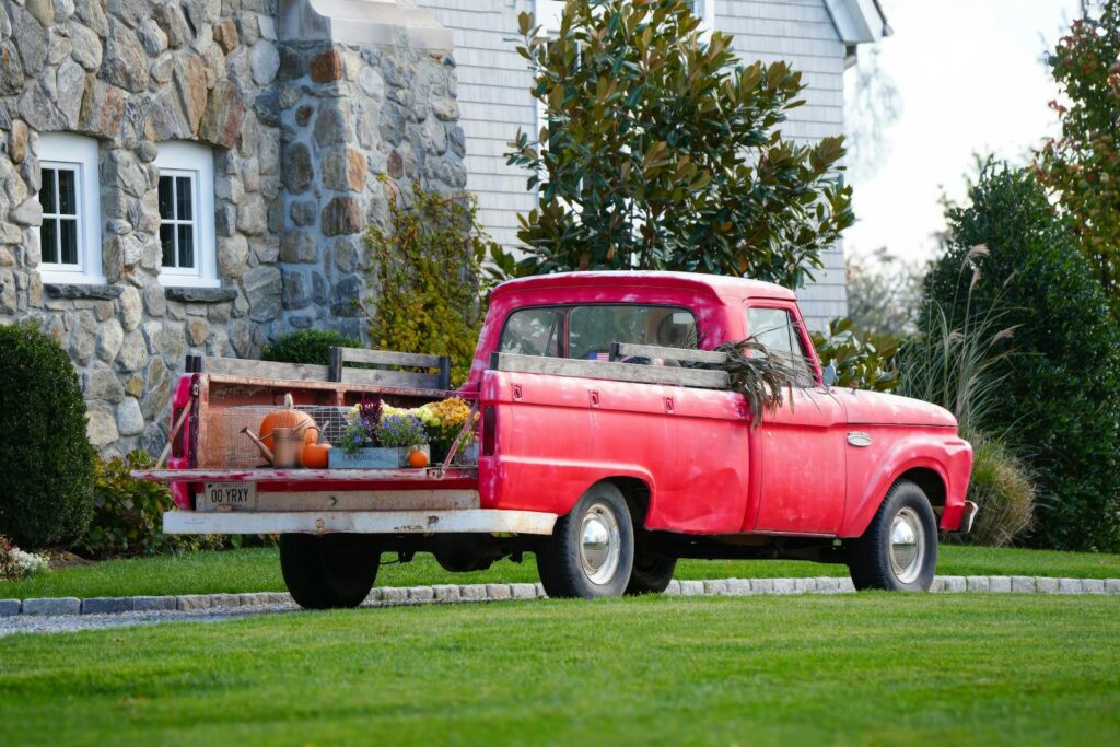 A classic red pickup truck adorned with garden tools and flowers in a picturesque outdoor setting.