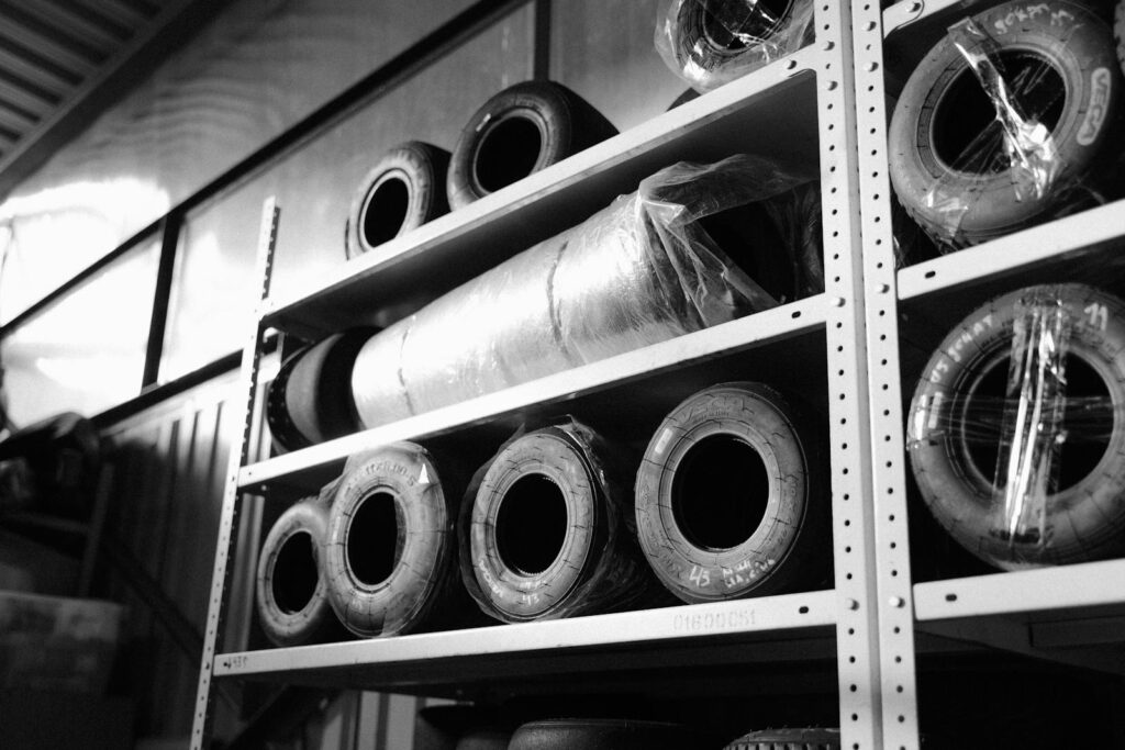 Black and white image of racing tires stored on metal shelves in a warehouse.