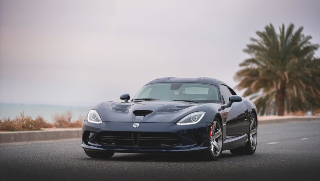 A luxury black Dodge Viper sports car parked on a road with palm trees in the background.