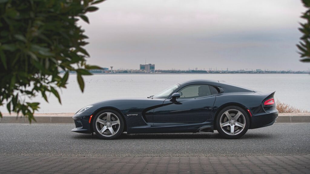 Luxurious black sports car parked by a waterfront road, showcasing elegance and modern design.