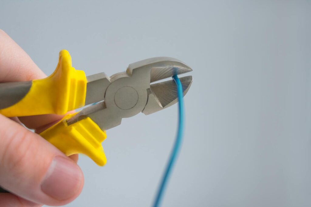 Detailed image of a hand using yellow-handled pliers to cut a blue wire.