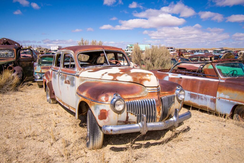 A collection of rusted vintage cars abandoned in a desert scrapyard under a clear sky.