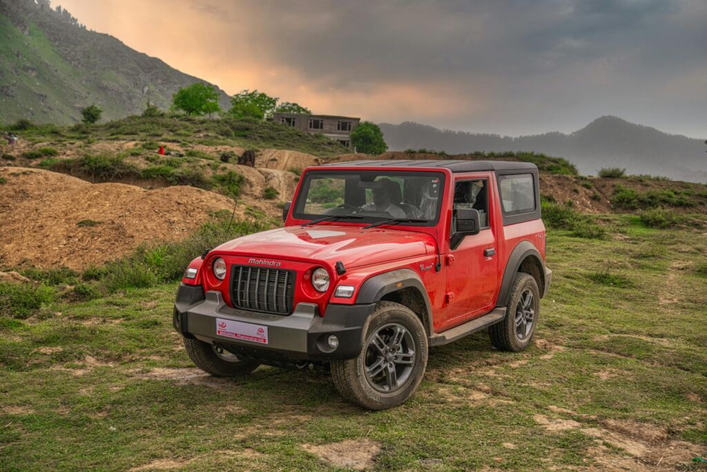 A vibrant red Mahindra Thar parked off-road in the scenic Dara mountain region of Kashmir.