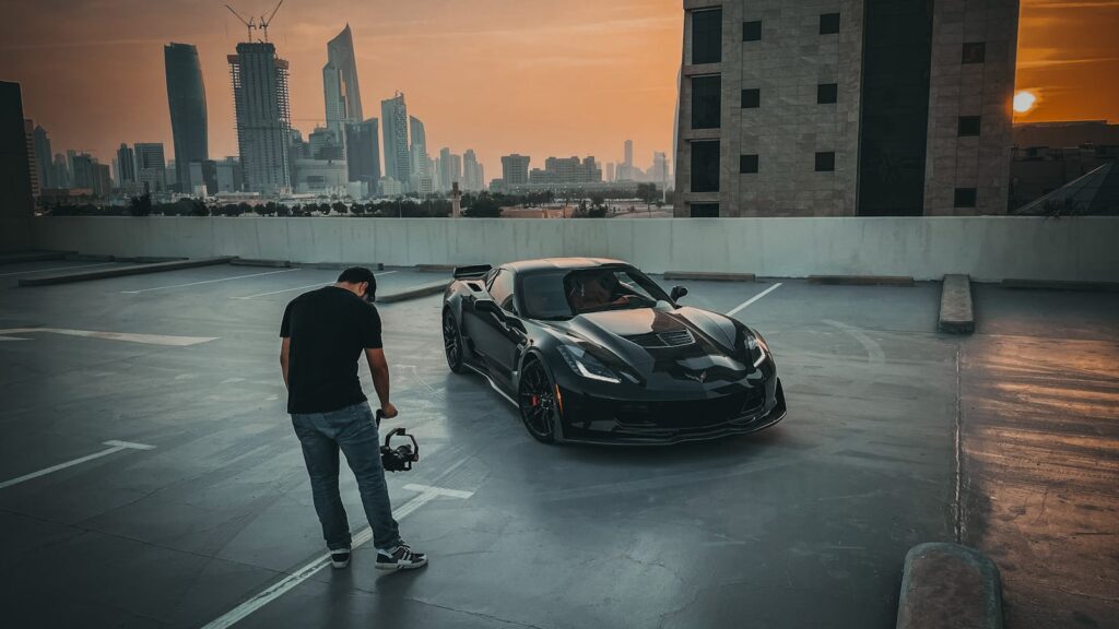 A Chevrolet Corvette being filmed at sunset on a rooftop with a city skyline background.