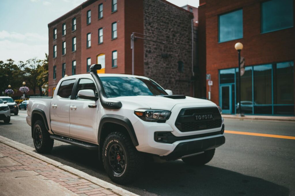 White Toyota pickup truck parked on a city street with red brick buildings.